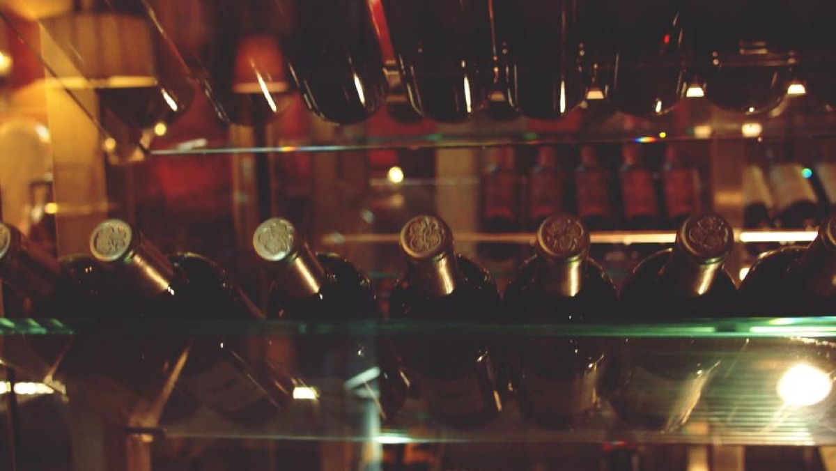 Backlit wine bottles resting on glass shelves in a dim tasting cellar